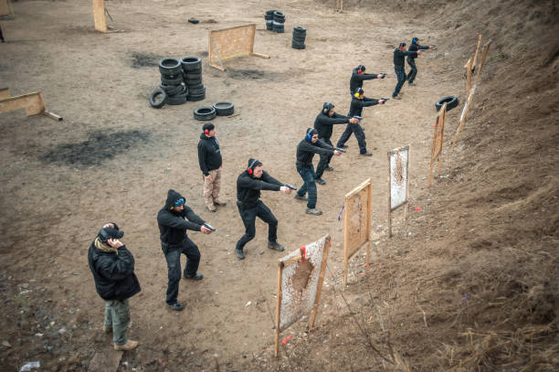 Large group of students with two instructors practice gun shooting on outdoor shooting range. Civilian team weapons training and course